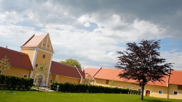 A yellow building with a red roof, surrounded by green grass and a tree.