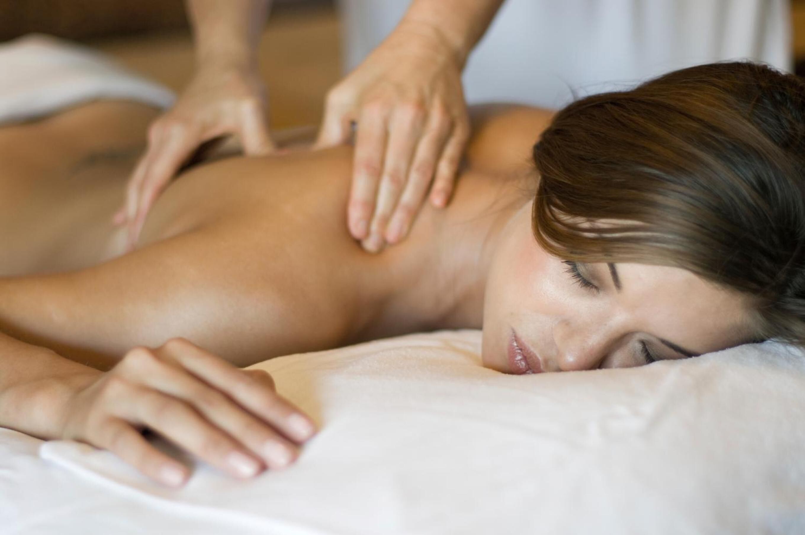 A person lying on a bed receiving a back massage.