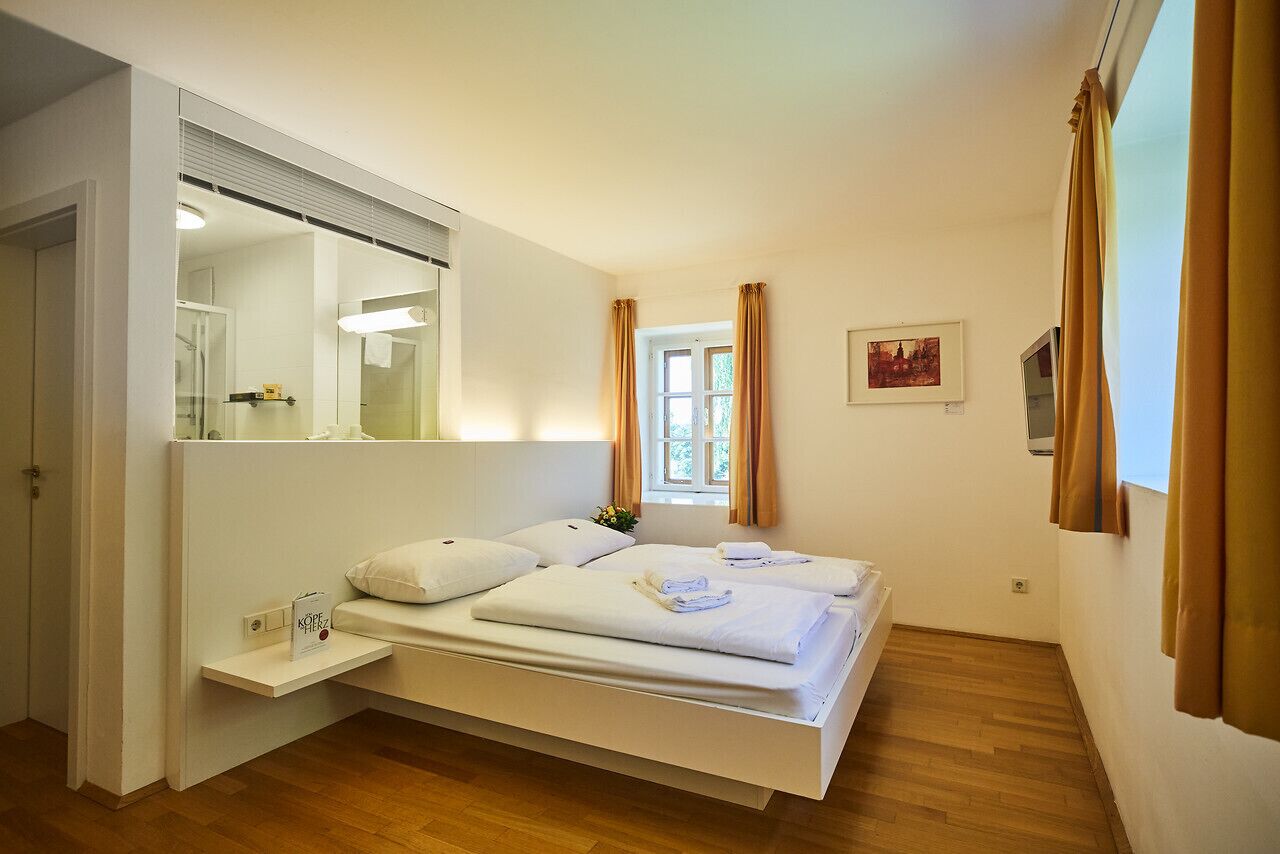 Un dormitorio moderno con una cama grande, una mesita de noche, un espejo, una ventana con cortinas y un cuadro pequeño en la pared.