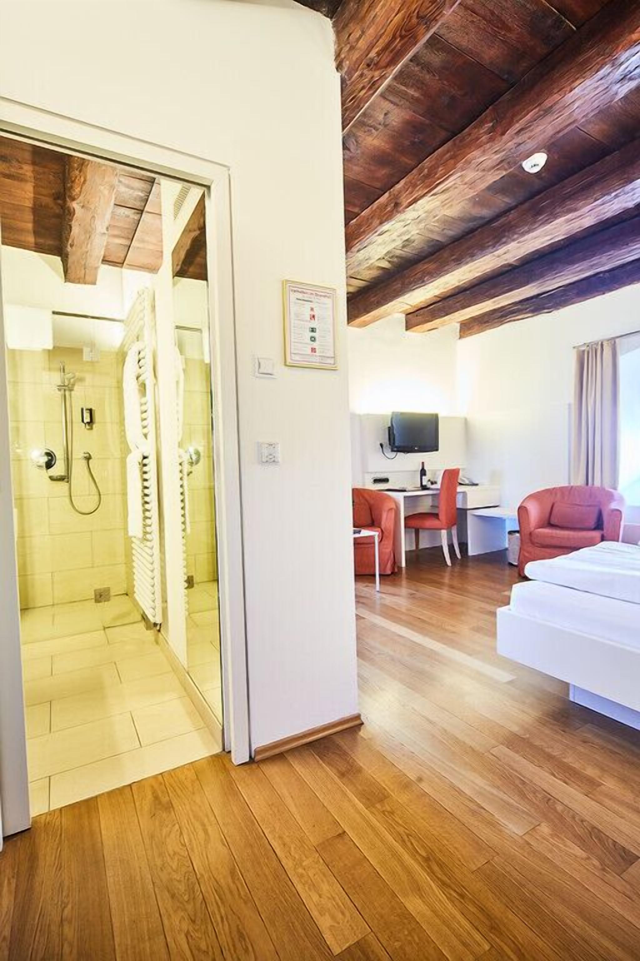 Habitació d'hotel amb sostre de fusta, un llit, escriptori i zona de dutxa.