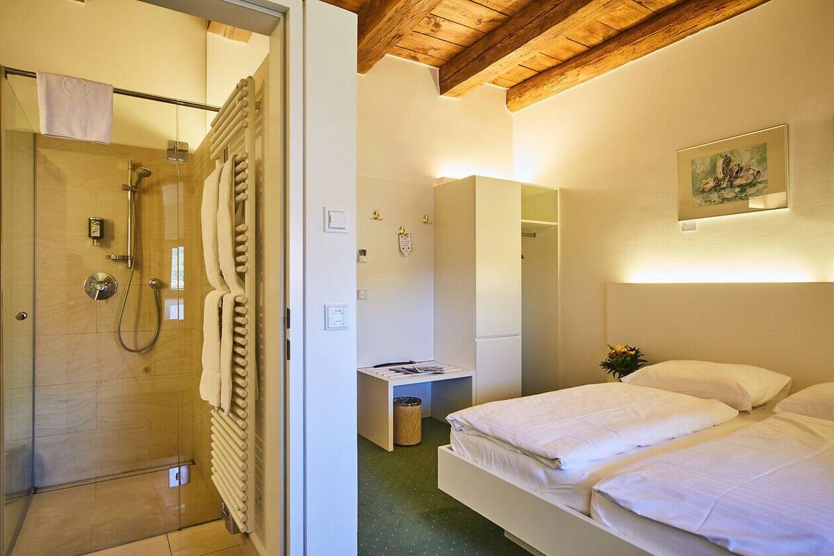 A hotel room with a shower, a bed, a desk, and a mirror.