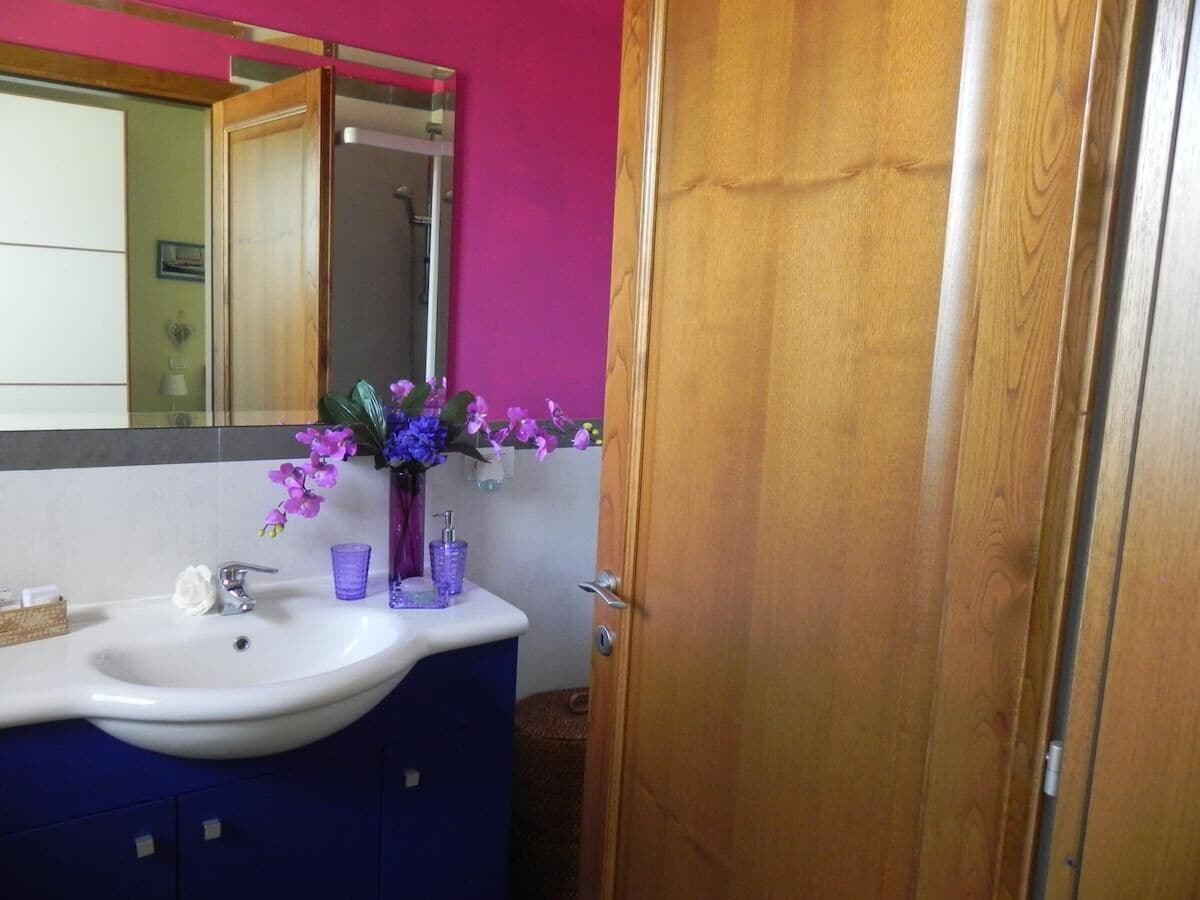 Un baño con un lavamanos blanco, flores moradas y una puerta de madera.