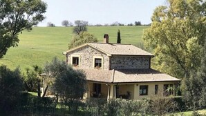 Una casa de piedra con techo de tejas, rodeada de follaje y árboles.