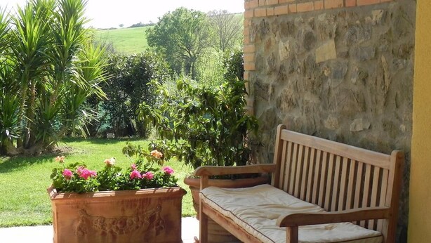 Un banco de madera con cojín, una pared de piedra y una maceta con flores.
