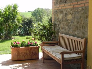 Un banco de madera con cojín, una pared de piedra y una maceta con flores.