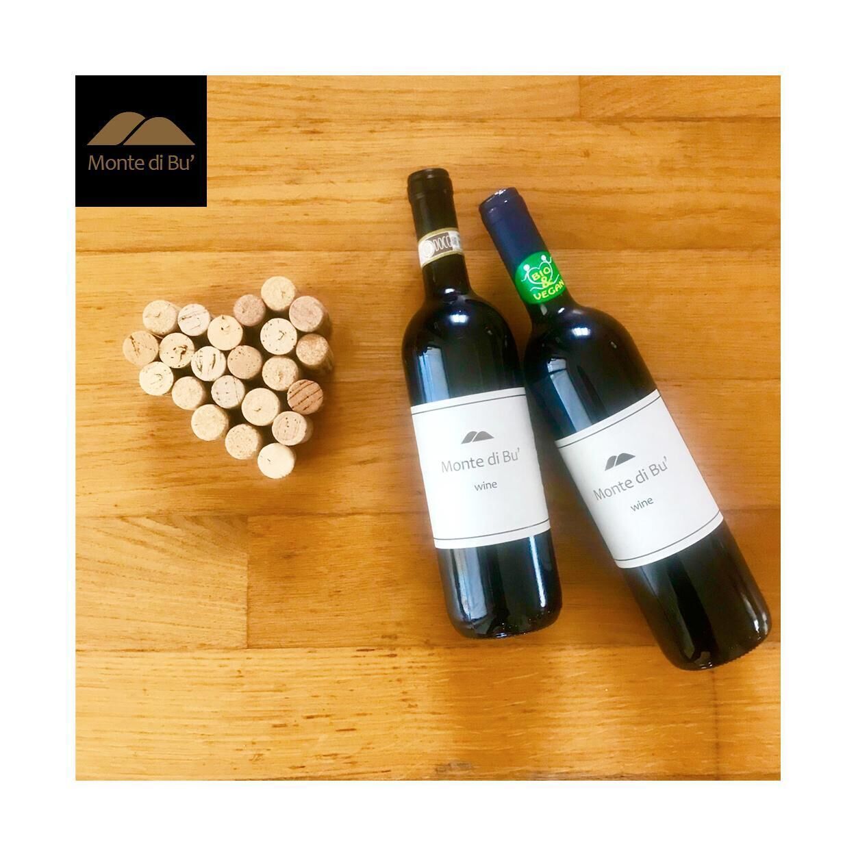 Two bottles of Monte di Bu' wine and a heart-shaped arrangement of wine corks on a wooden surface.