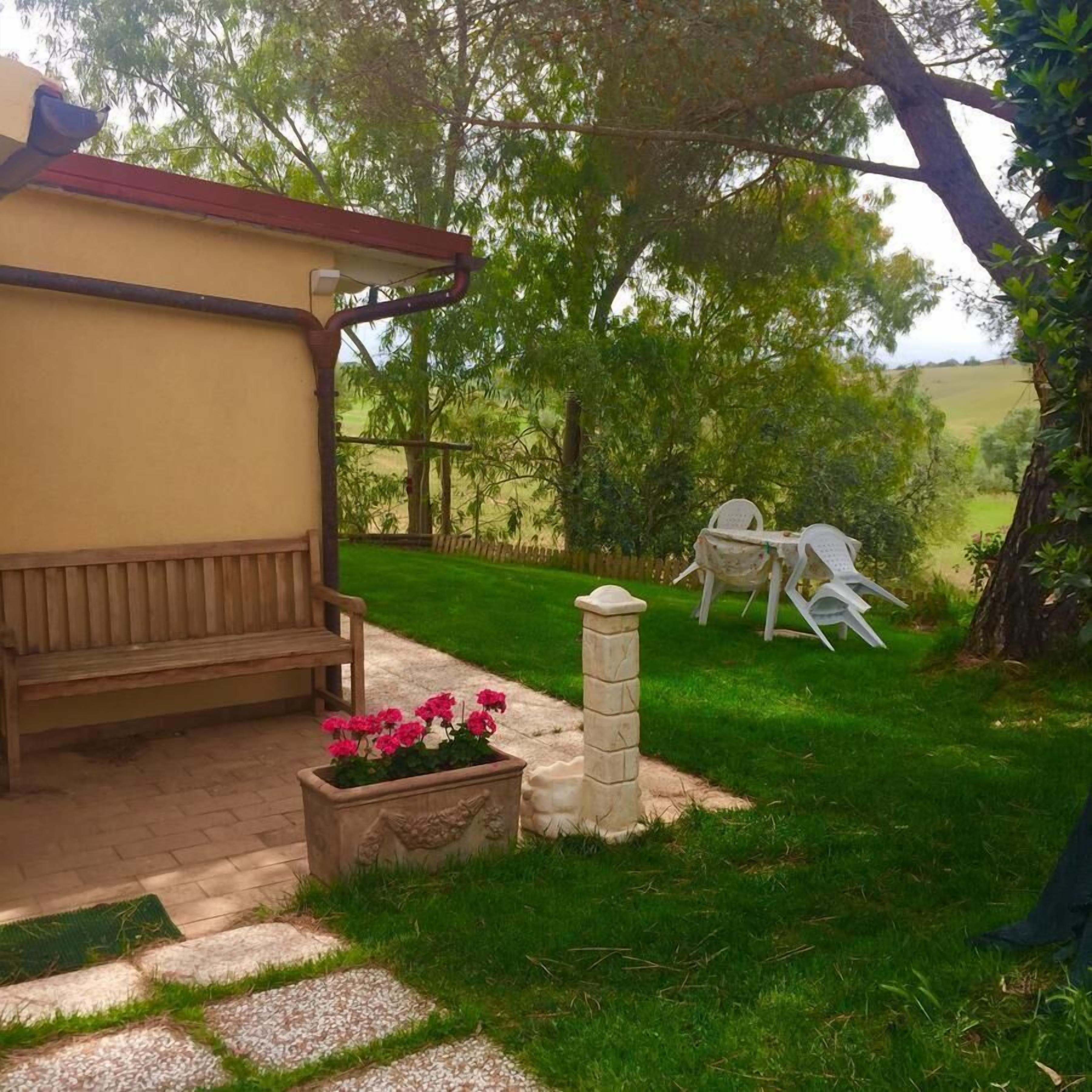 Eine Terrasse mit einer Holzbank, einem Steinpflanzgefäß mit Blumen und einem weißen Stuhl.