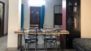 A dining area with a wooden table and four chairs, a dark cabinet with glass doors, and a blue curtain. - Utsav Bed & Breakfast (Noida)
