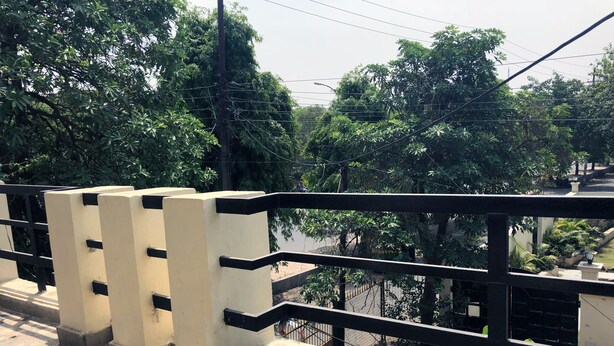A balcony with a black railing, beige pillars, and a patterned floor. - Utsav Bed & Breakfast (Noida)