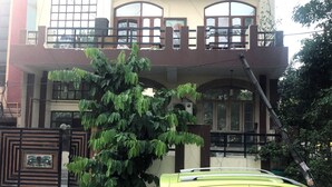 A two-story building with a gated entrance, a large tree in front, and a parked car. - Utsav Bed & Breakfast (Noida)
