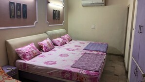 A bedroom with a bed, pillows, a bedside table, a wardrobe, and an air conditioning unit. - Utsav Bed & Breakfast (Noida)