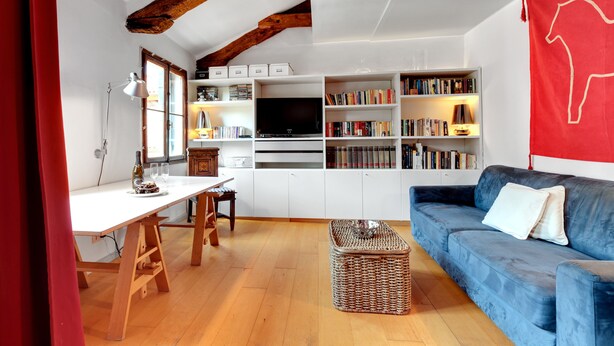 A living room with a white TV stand, bookshelves, a blue sofa, and a wooden table. - Bragora Smoochy Attic Venice (Venice)