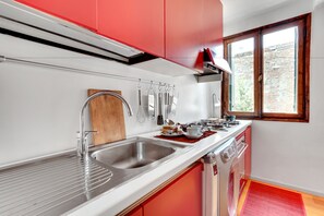 A modern kitchen with red cabinets, stainless steel appliances, and a window providing natural light.