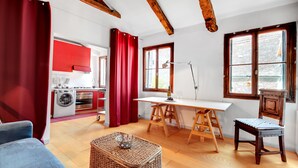 A room with a wooden ceiling, a dining table with chairs, a kitchen area with red cabinets, and a window with a view. - Bragora Smoochy Attic Venice (Venice)