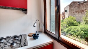 A kitchen with a gas stove, a red cabinet, a window with a view of greenery and buildings, and a wooden door. - Bragora Smoochy Attic Venice (Venice)