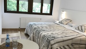 A bedroom with two beds, a table with glasses and a water bottle, a chair, and a window with blinds. - El Malecon (Sarria)