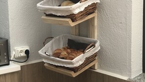 A corner shelf unit with woven baskets containing bread and pastries. - El Malecon (Sarria)