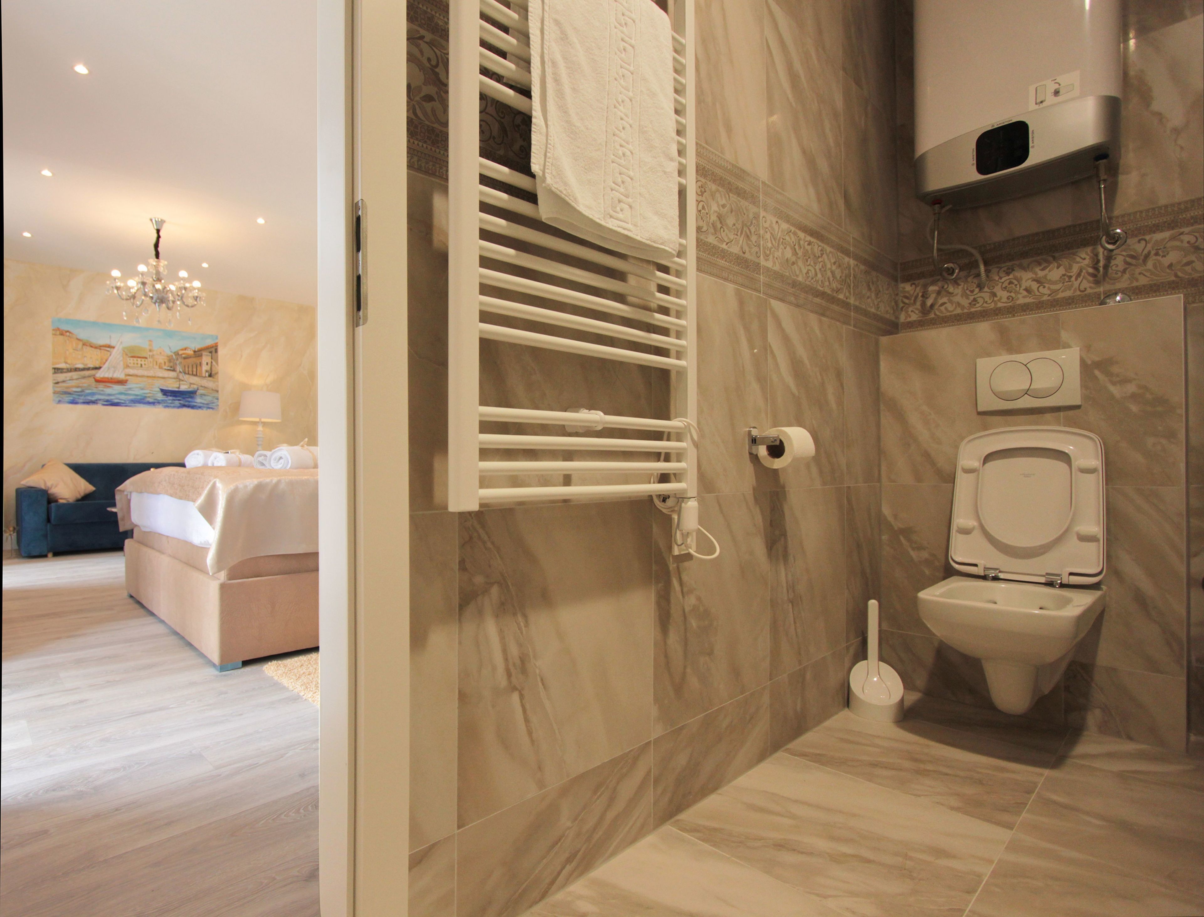 Un baño moderno con piso de mármol, inodoro blanco, toallero y zona de ducha.
