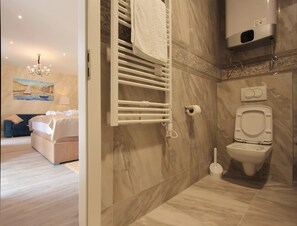Ein modernes Badezimmer mit Marmorboden, Toilette in Weiß, einem Handtuchhalter und einer Duschkabine.