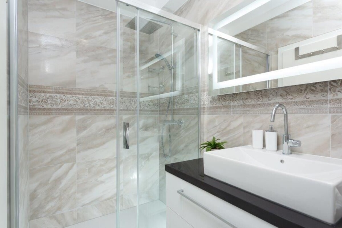 Une salle de bain moderne avec une douche à parois de verre, un lavabo blanc et un miroir au-dessus.