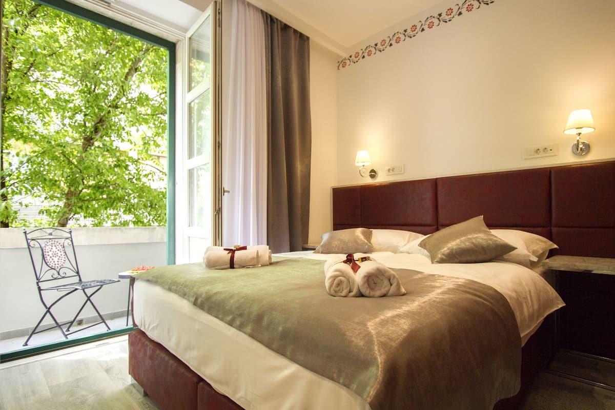 A hotel room with a bed, a chair, a window with curtains, and a wall with a floral design.