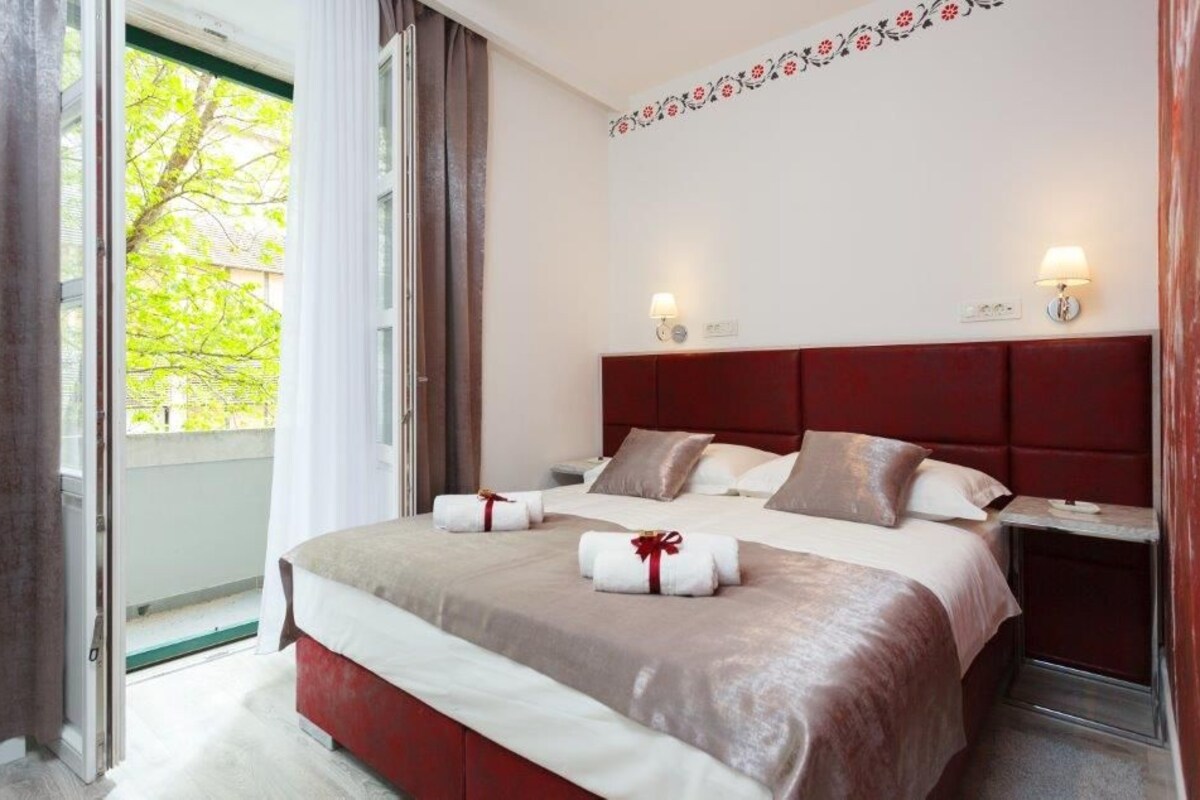 A hotel room with a large bed, a nightstand, a window with curtains, and a decorative floral wall design.