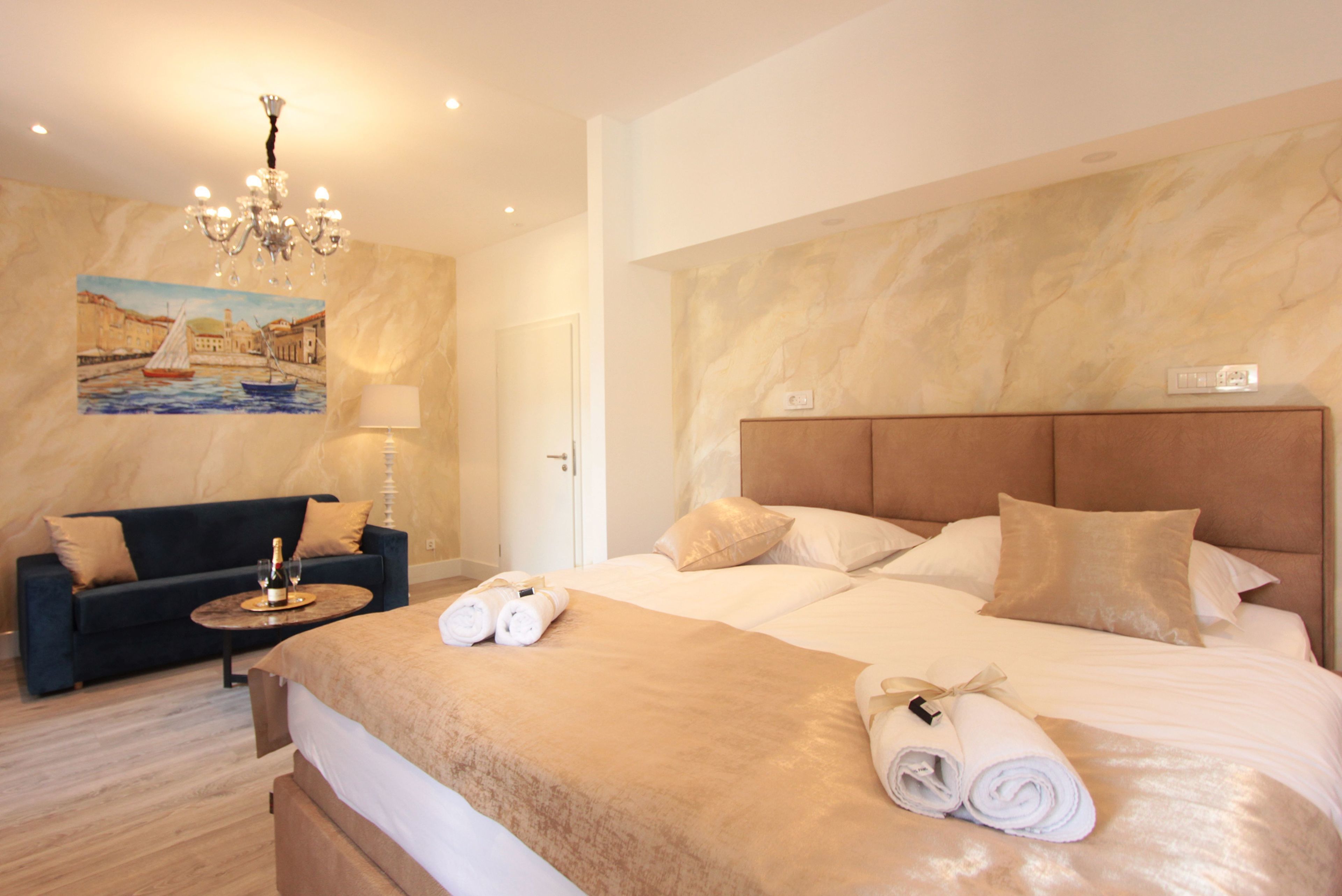 Hotelkamer met een groot bed, een hoofdeinde, een schilderij van een zeilboot, een kroonluchter, een bank en een tafel met een fles en glazen.