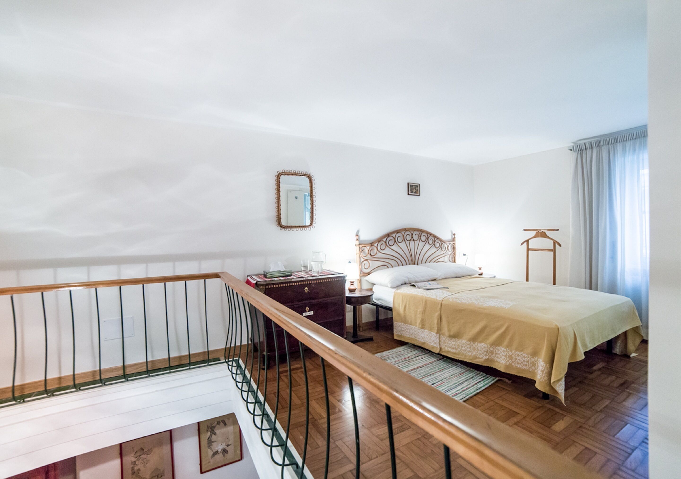 A bedroom with a wooden bed, a nightstand, a dresser, a mirror, and a window with curtains.