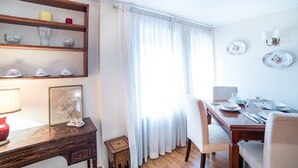 Un coin repas avec une table en bois dressée pour quatre personnes, une petite table d’appoint avec une lampe rouge et une étagère ornée d’objets décoratifs.