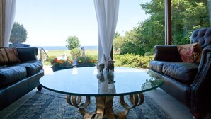 A room with two leather sofas facing a glass coffee table, a wooden table base, and a view of the sea through large windows. - Sunny Brae (Nairn)