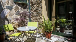 An outdoor seating area with a table and chairs, surrounded by potted plants and a stone wall. - Pension Siete en el Camino (Sarria)