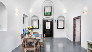 A dining area with a table set for four, a black door, and arched white walls. - Casa d'Argento (Santorini)