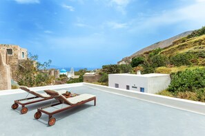 A rooftop terrace with two sun loungers, a view of the sea, and traditional architecture in the background. - Casa d'Argento (Santorini)
