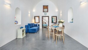 A spacious living area with a blue sofa, a dining table with chairs, and a small white cabinet. - Casa d'Argento (Santorini)