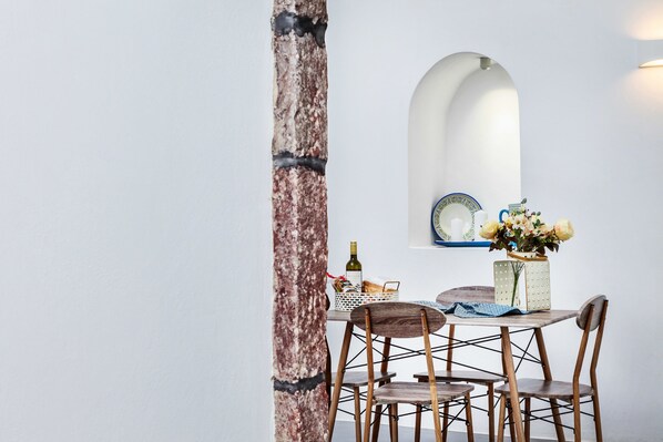 A dining area with a rustic wooden table, chairs, a vase with flowers, and a mirror on the wall. - Casa d'Argento (Santorini)