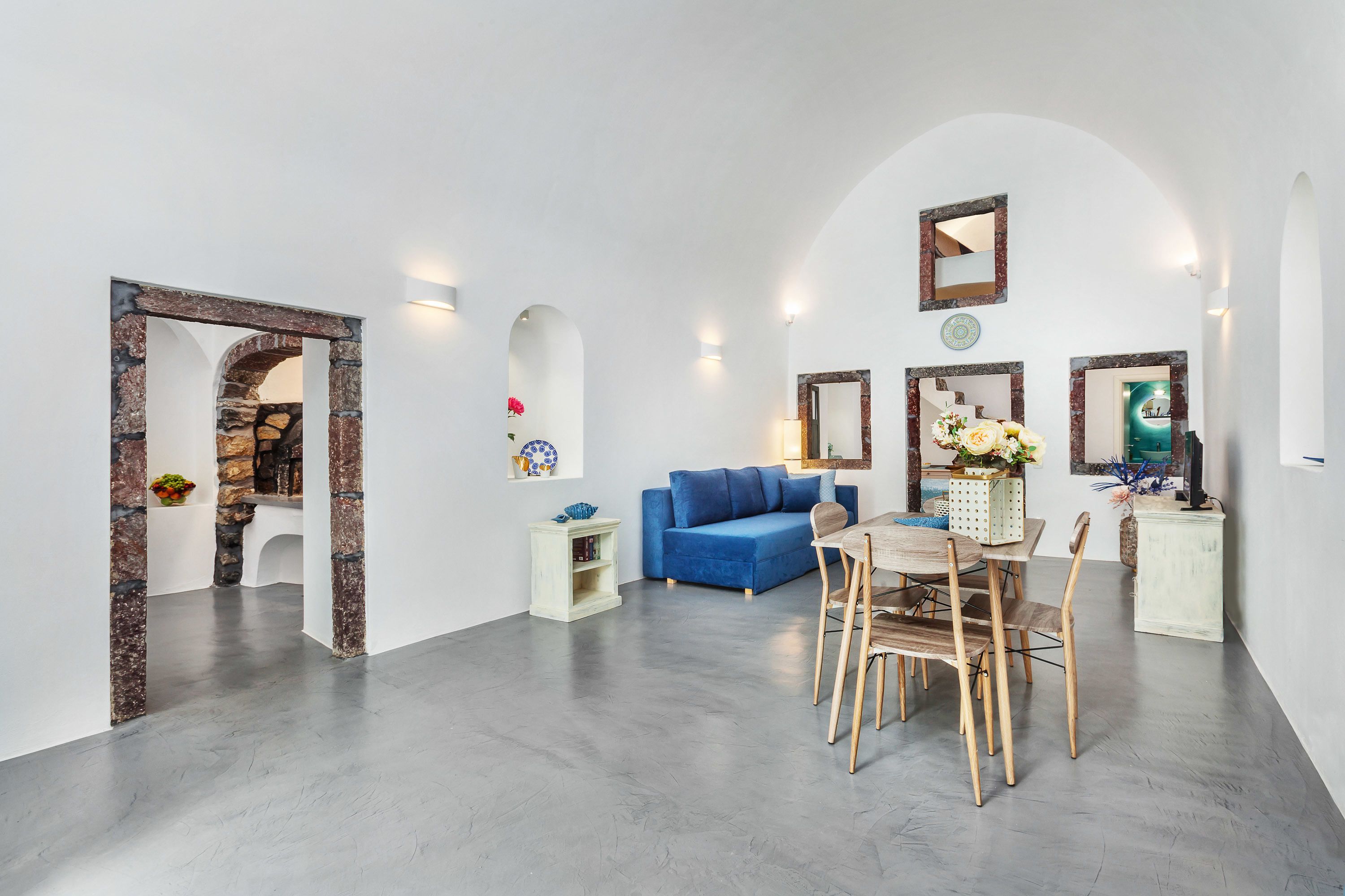 Una sala de estar moderna con un sofá azul, una mesa de comedor con sillas y una zona de cocina con estufa.