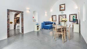 A modern living room with a blue sofa, a dining table with chairs, and a kitchen area with a stove. - Casa d'Argento (Santorini)