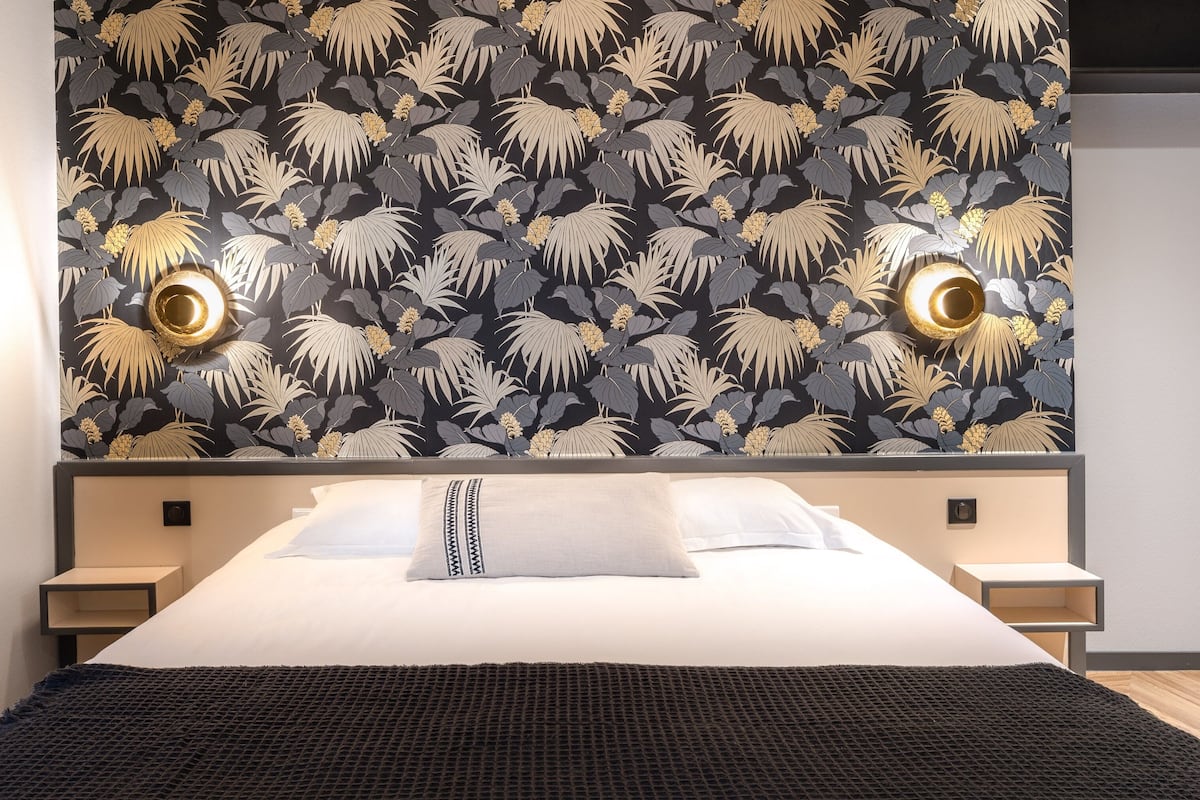 A modern hotel room with a large bed, two bedside tables, and a wall with a leaf-pattern wallpaper.
