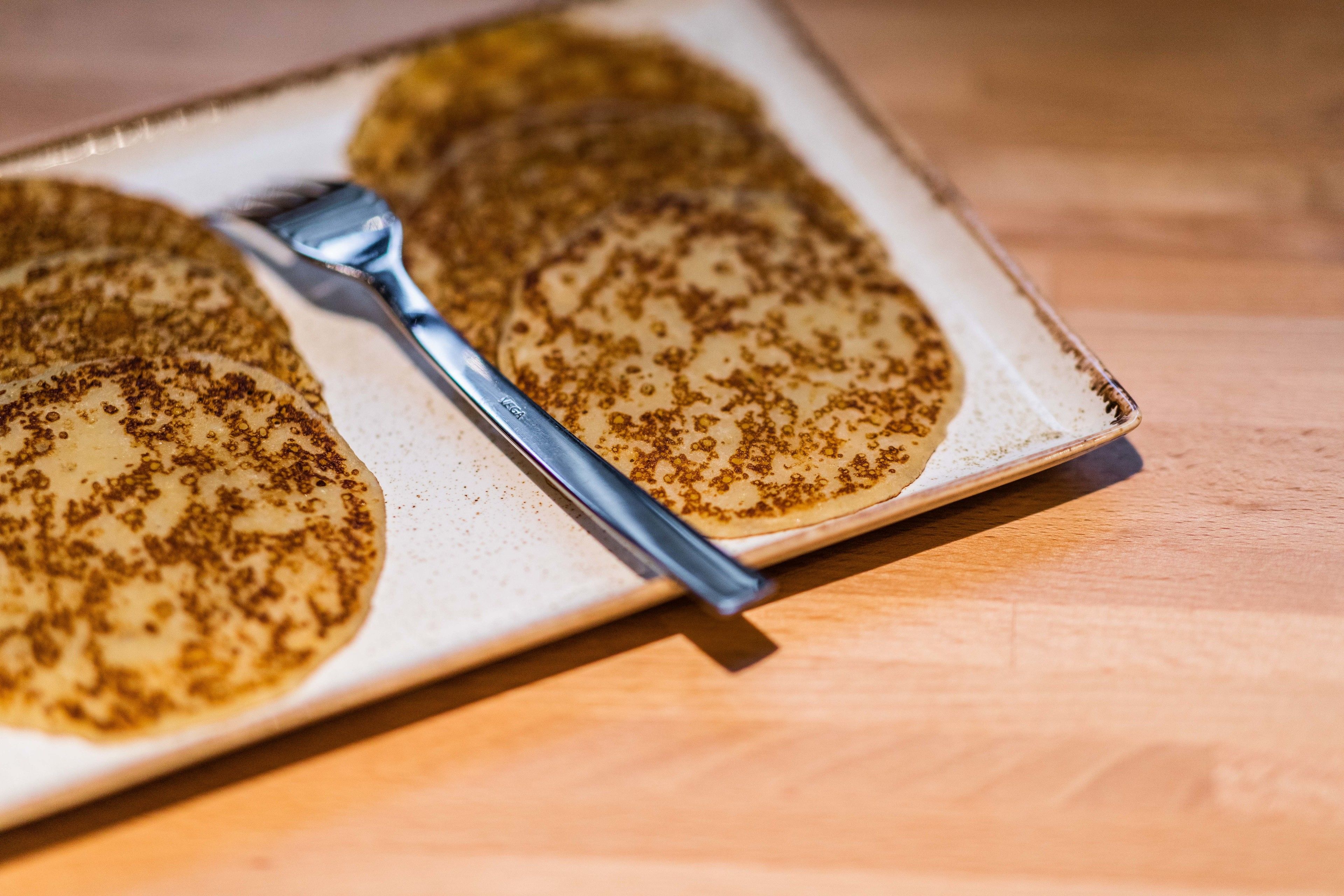 Un piatto con diverse crespelle e una forchetta su un tavolo di legno.