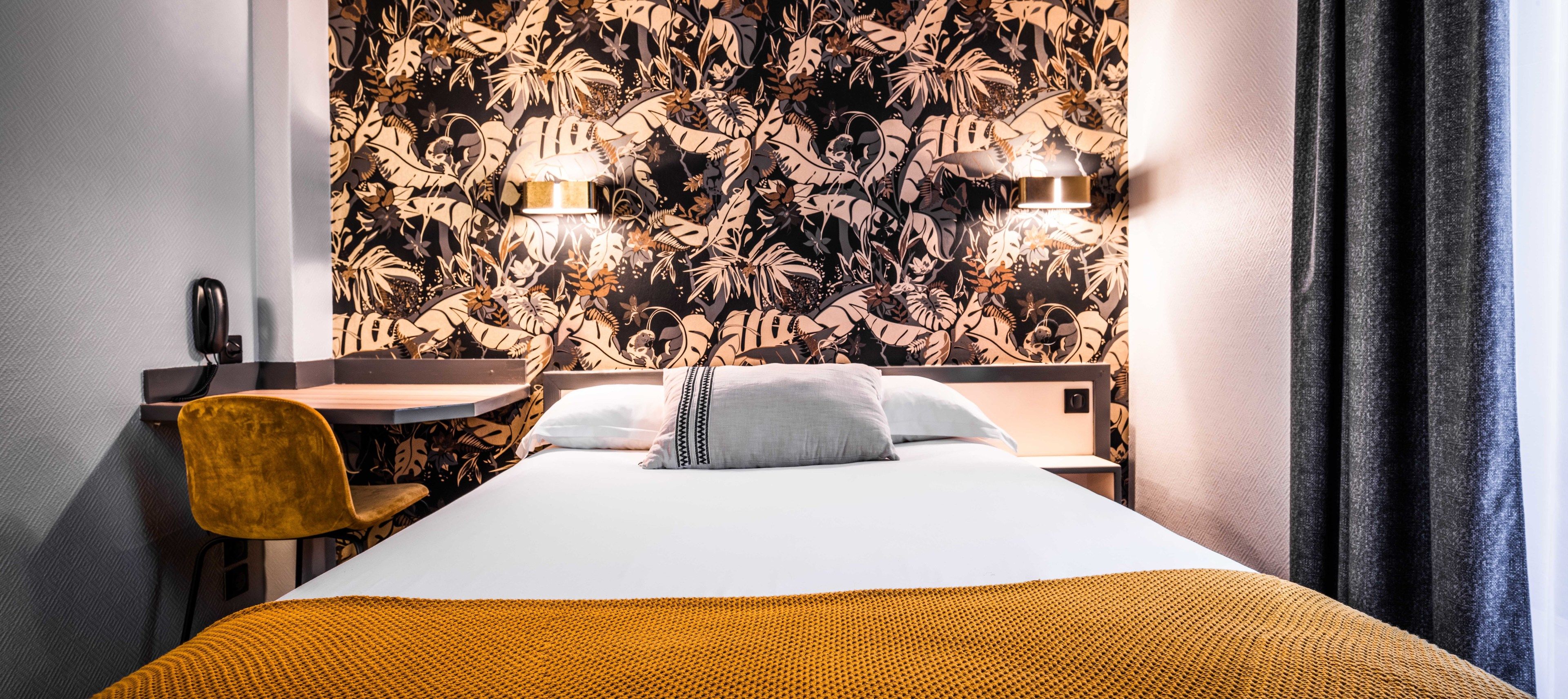 A hotel room with a bed, a desk, and two wall-mounted lamps.