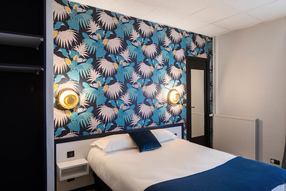A hotel room with a bed, a nightstand, a mirror, and a window with curtains.