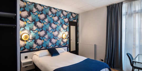 Habitación de hotel con cama, mesita de noche, espejo y ventana con cortinas.