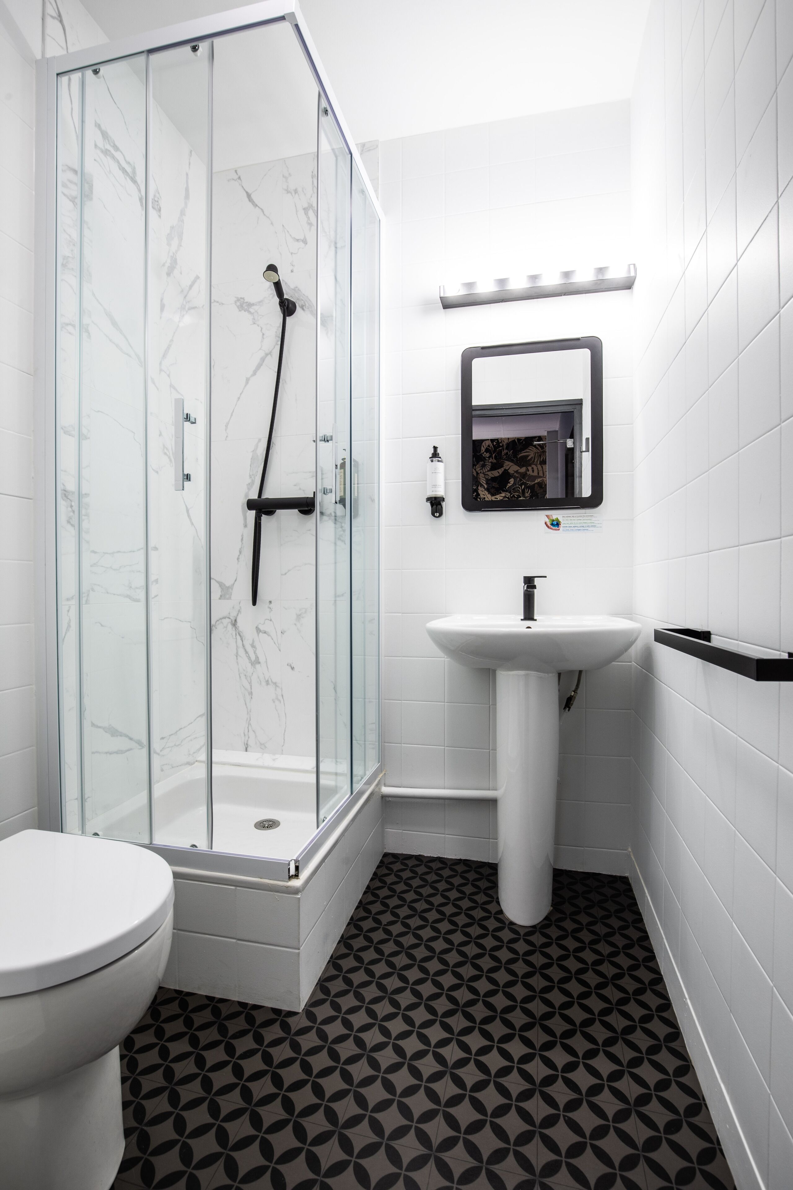 Un bany modern amb dutxa tancada per vidre, un lavabo blanc i un vàter.