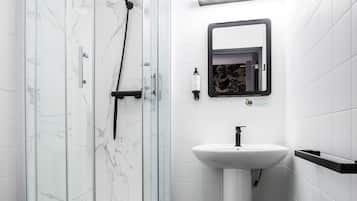 Un bany modern amb dutxa tancada per vidre, un lavabo blanc i un vàter.
