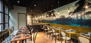 L’intérieur d’un restaurant est agrémenté de tables en bois, de chaises rembourrées et d’une fresque représentant une scène de forêt sur un mur.