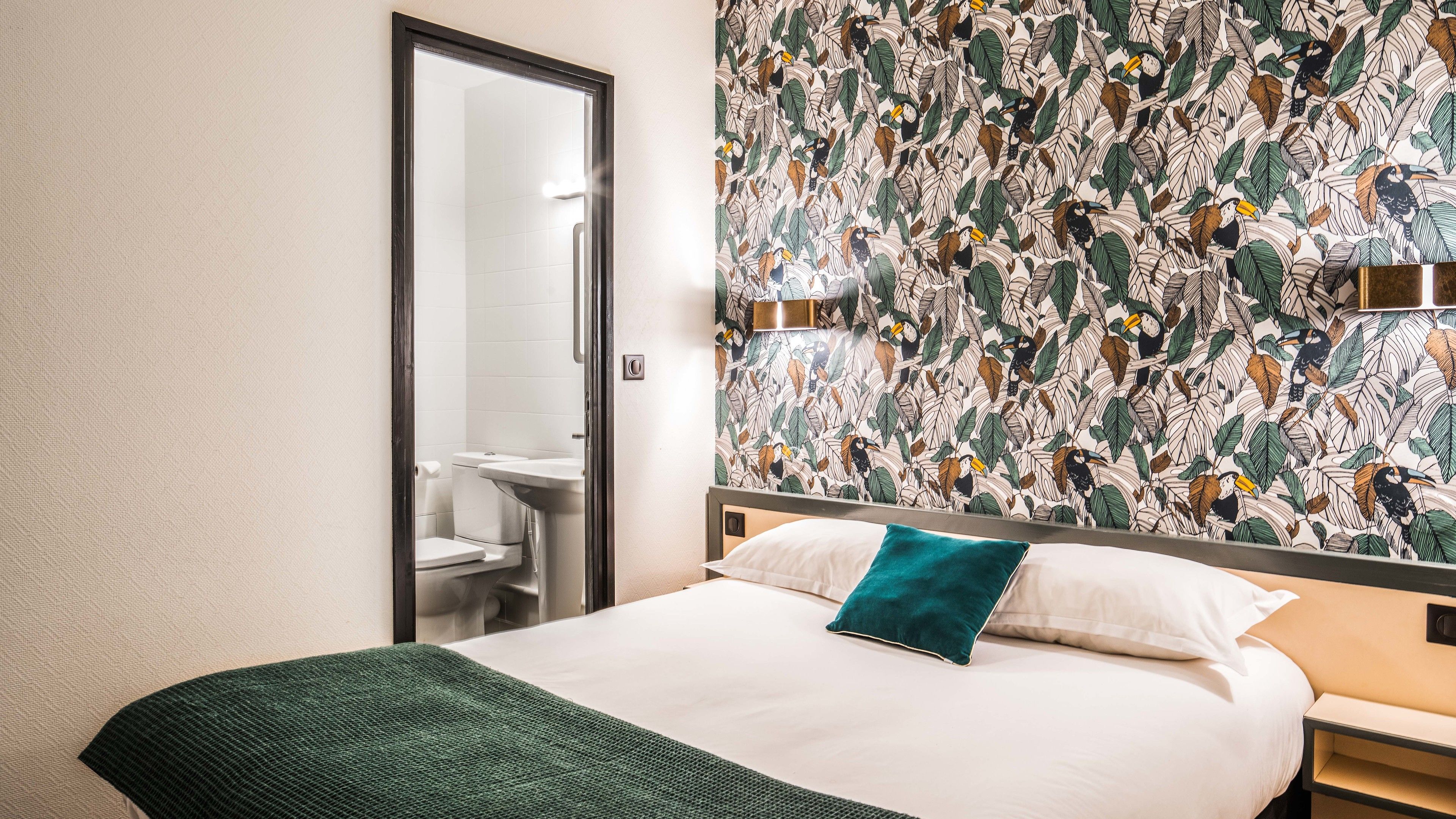 A hotel room with a bed, a bathroom with a toilet and sink, and a mirror.