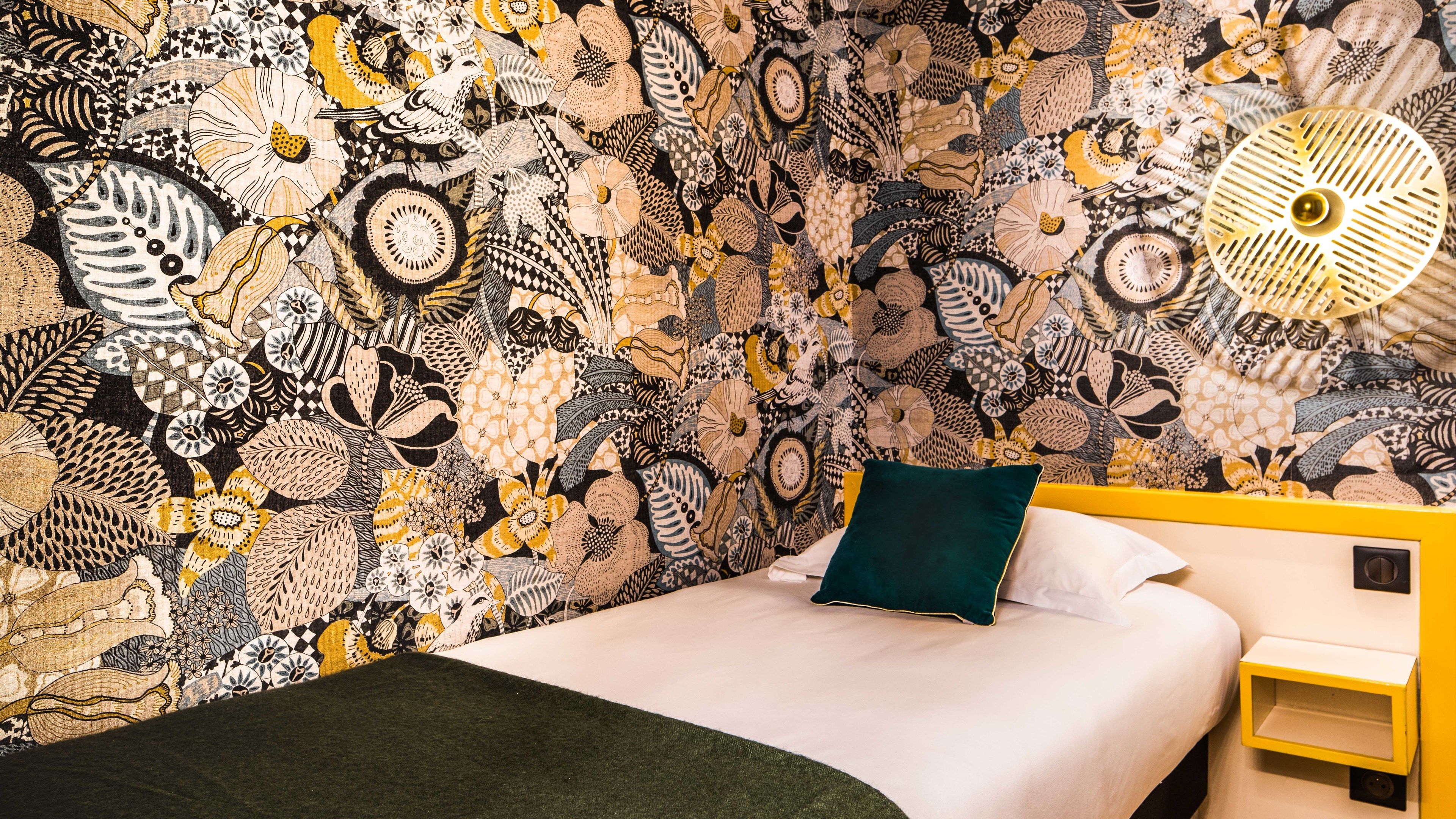 A room with a patterned wallpaper, a bed with a green pillow, and a yellow bedside table.