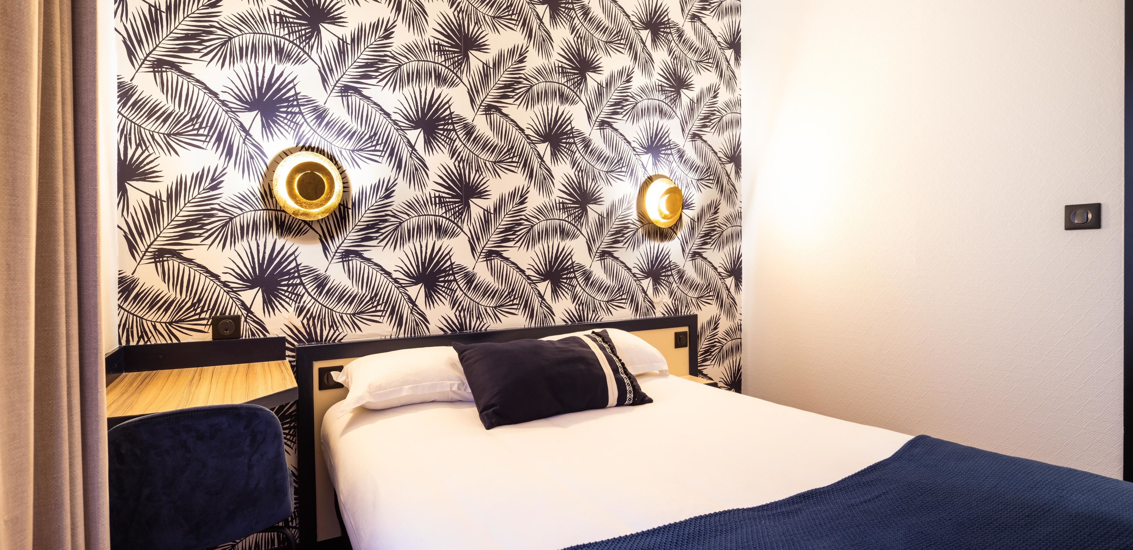 A hotel room with a bed, two wall-mounted lights, and a patterned wallpaper.