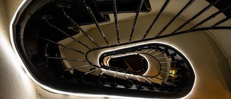 Una escalera en espiral con barandilla negra y una tira de luz a lo largo de la pared.