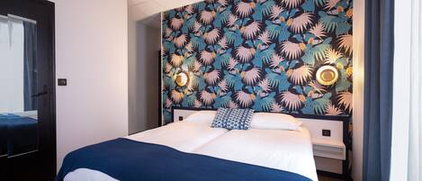 A hotel room with a bed, a nightstand, and a wall with a tropical leaf pattern.